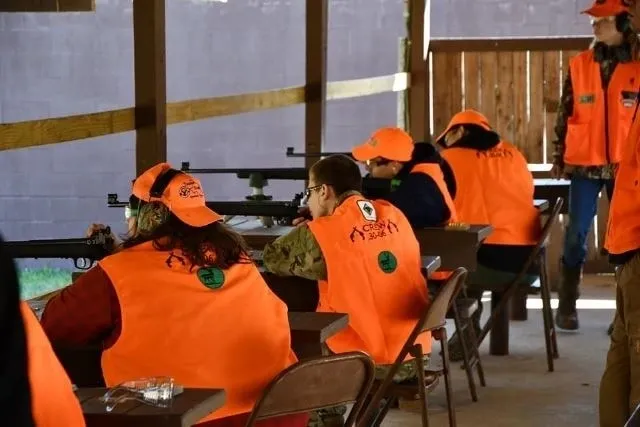 A group of people sitting at tables wearing orange vests.