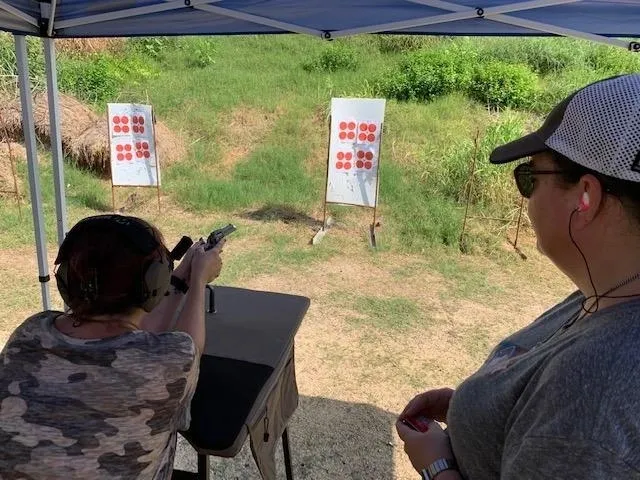 A man and woman shooting guns at an outdoor range.