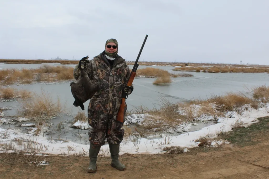 A man in camouflage holding a gun and wearing hunting gear.