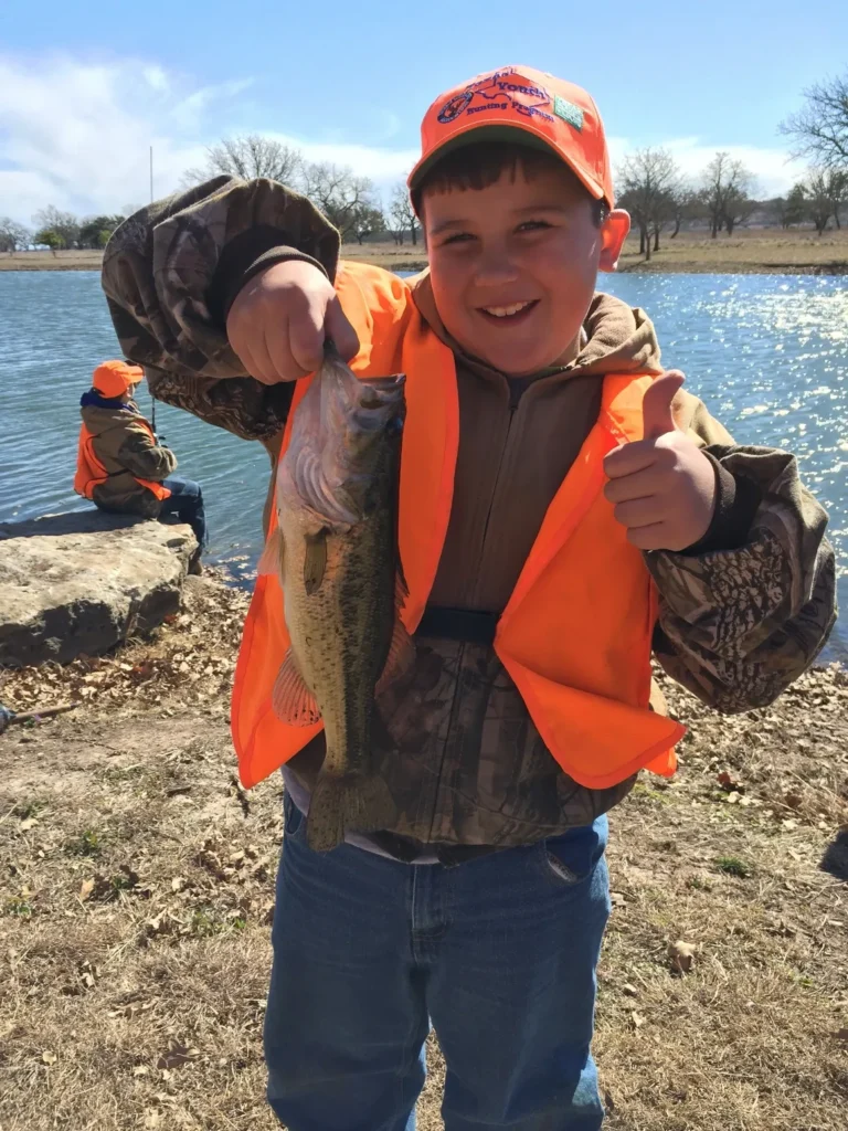 A young boy holding up a fish in his hand.