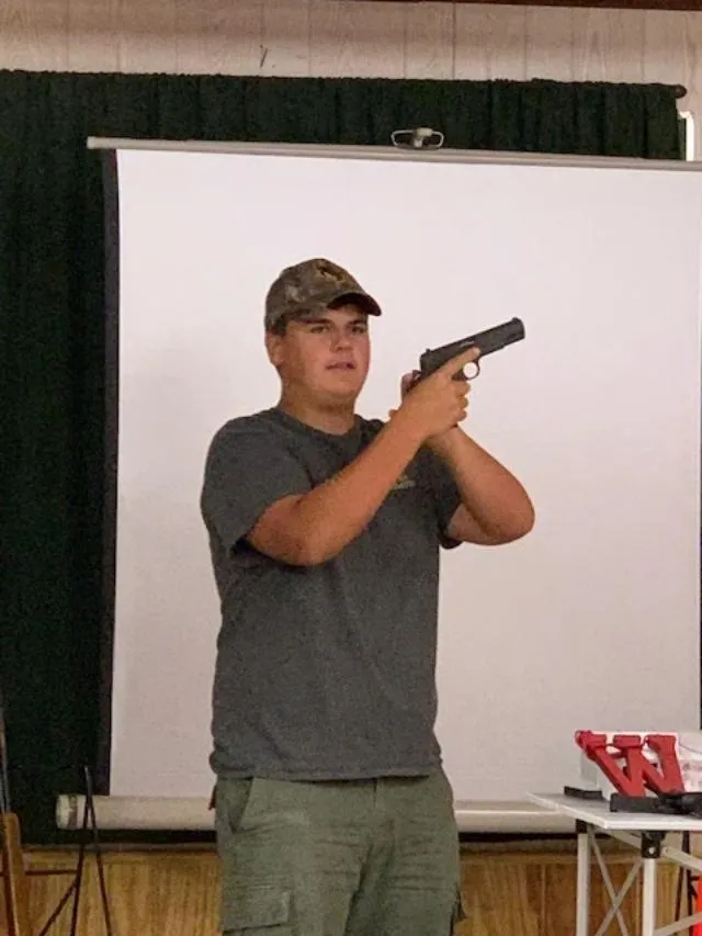 A man holding a gun in front of a white wall.