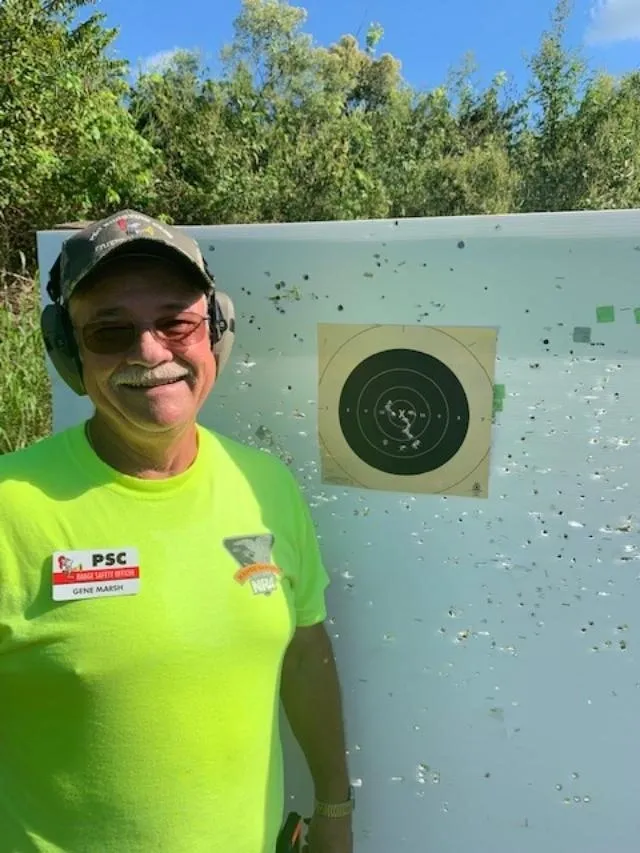 A man in a yellow shirt and ear muffs standing next to a target.