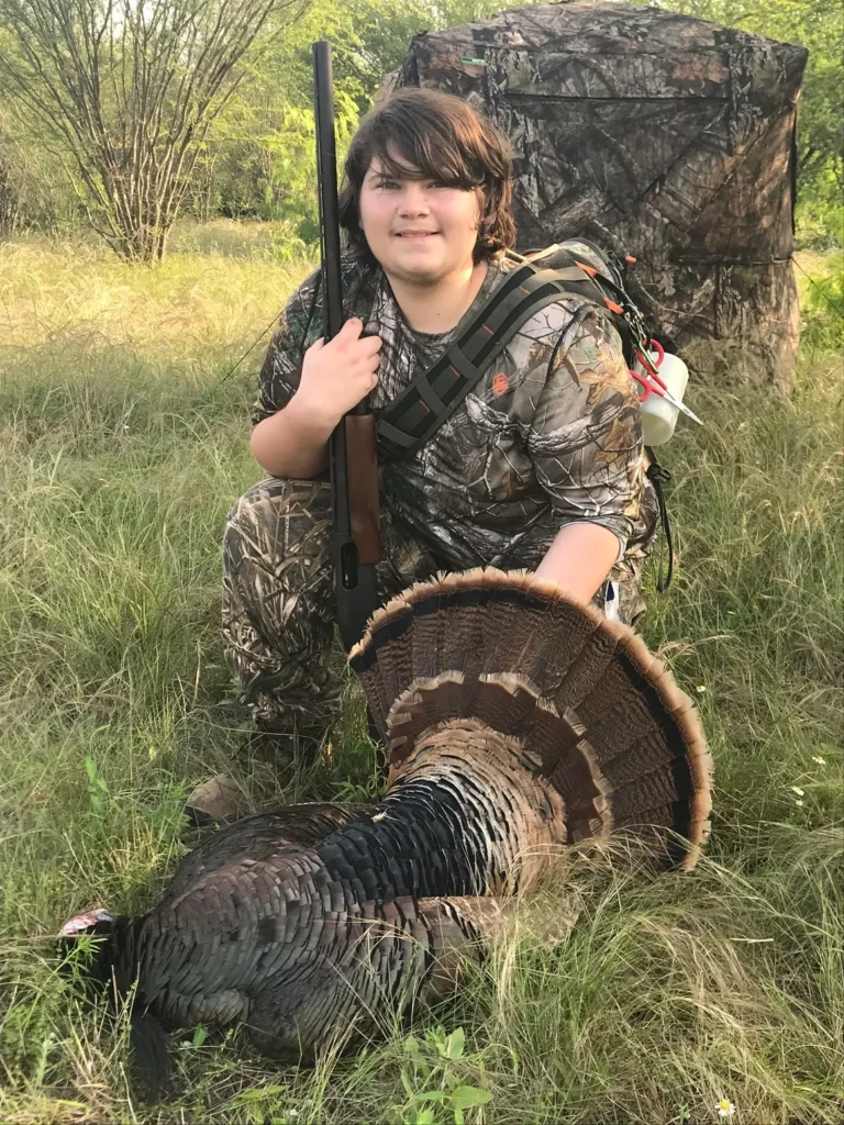 A boy in camouflage kneels next to a turkey.