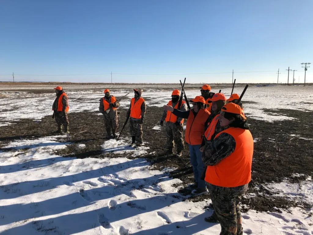 A group of people in orange vests standing on top of snow covered ground.