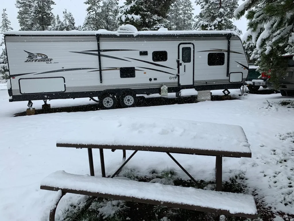A white rv parked in the snow next to a picnic table.