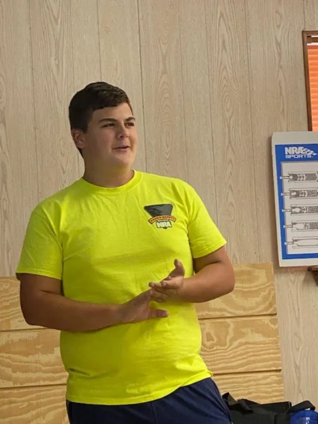 A man in yellow shirt standing next to wooden wall.