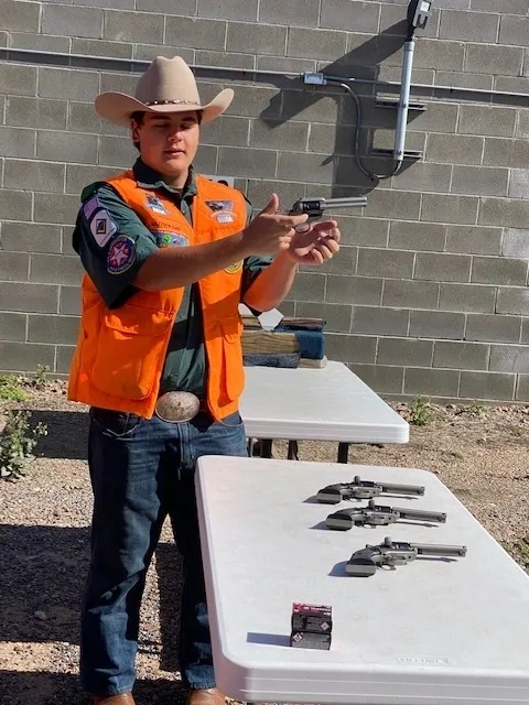 A man in an orange vest holding up two guns.