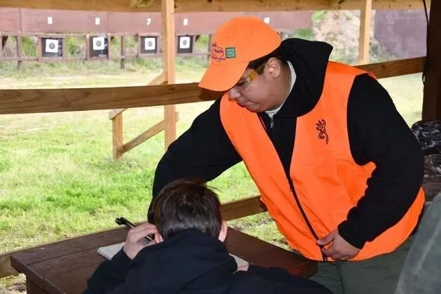 A man in an orange vest is pointing to something on the ground.