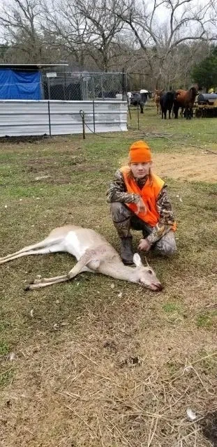 A young boy kneeling down next to dead deer.