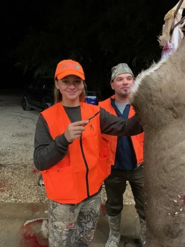 Two people in orange vests standing next to a large animal.