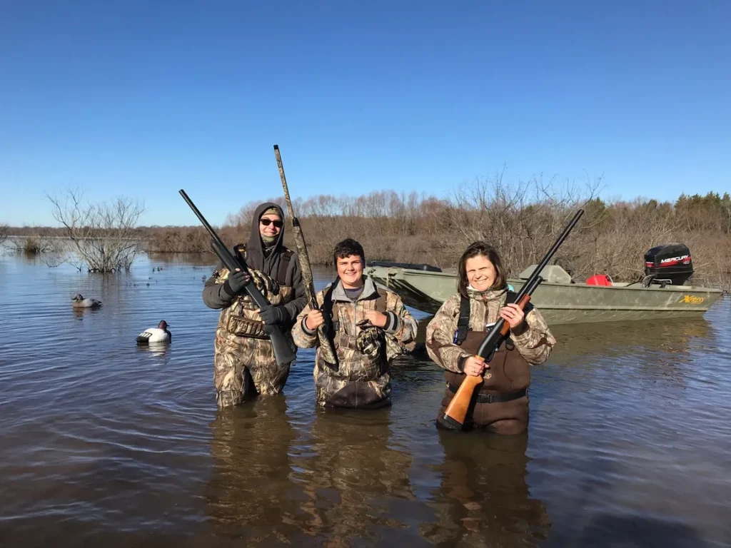 Three people in camouflage holding guns while standing in water.