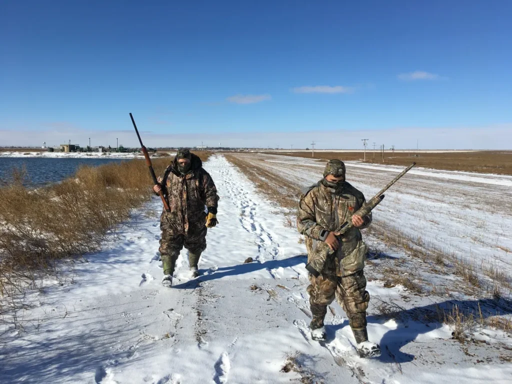Two hunters walking in the snow with guns.