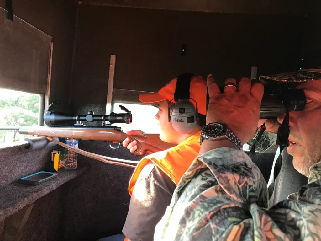 A man in orange vest holding rifle and wearing ear muffs.