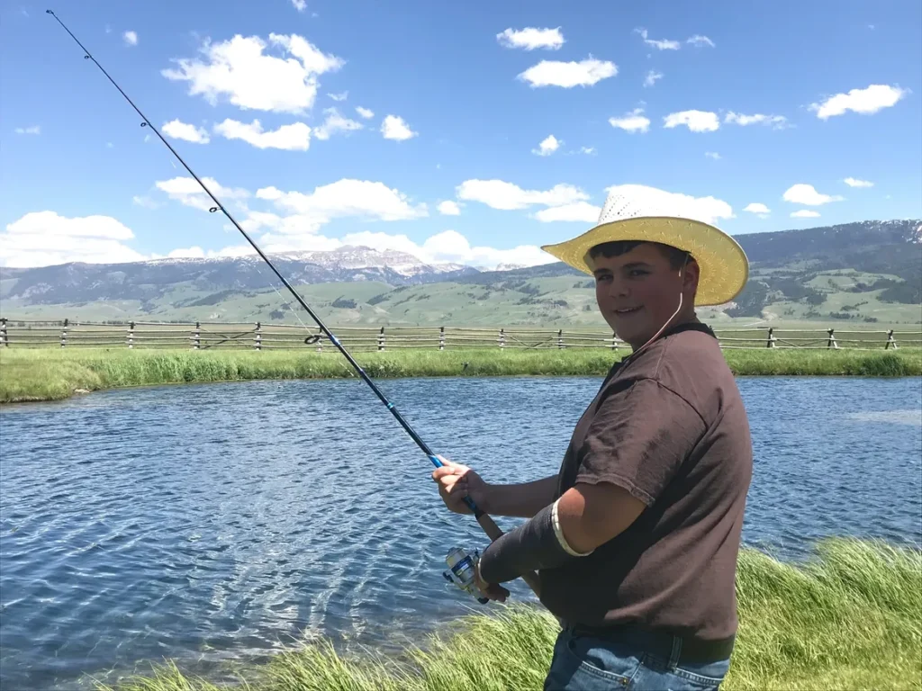 A man in cowboy hat holding fishing rod near water.