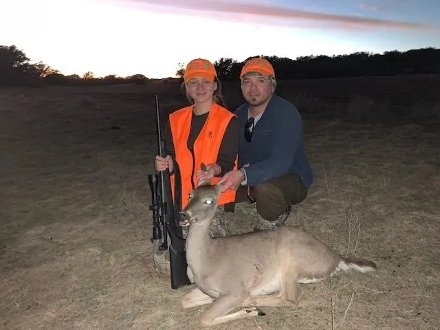Two people posing with a deer and guns.
