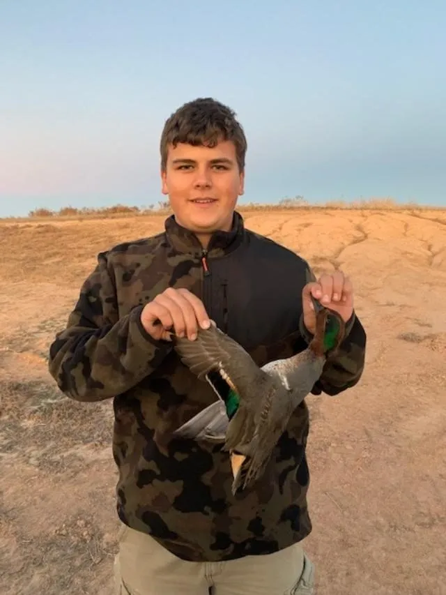 A young man holding a duck decoy in his hands.