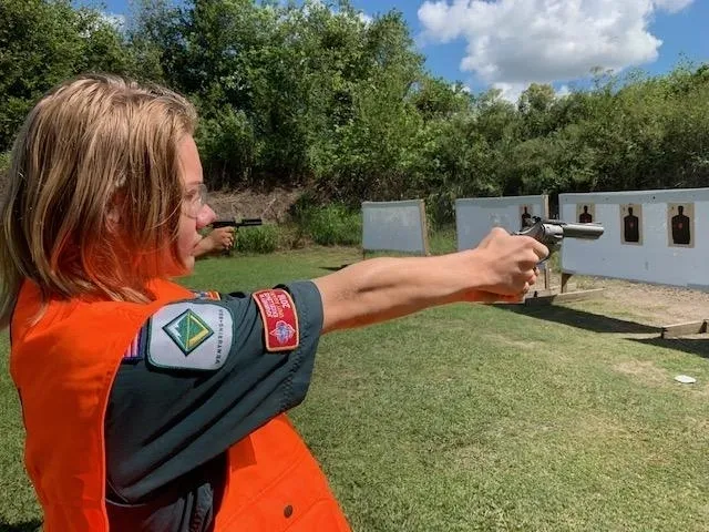 A woman is aiming at an object with her gun.