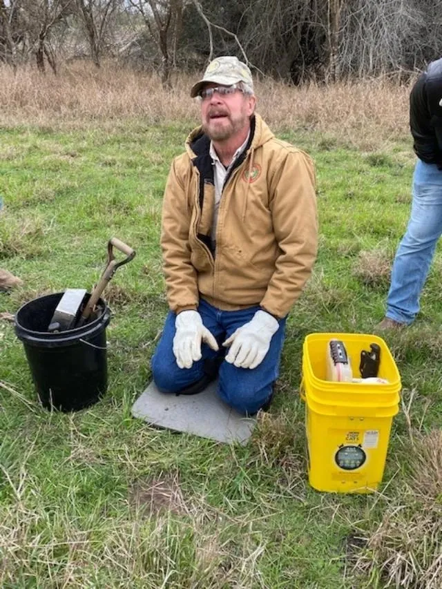 A man kneeling down next to buckets of trash.