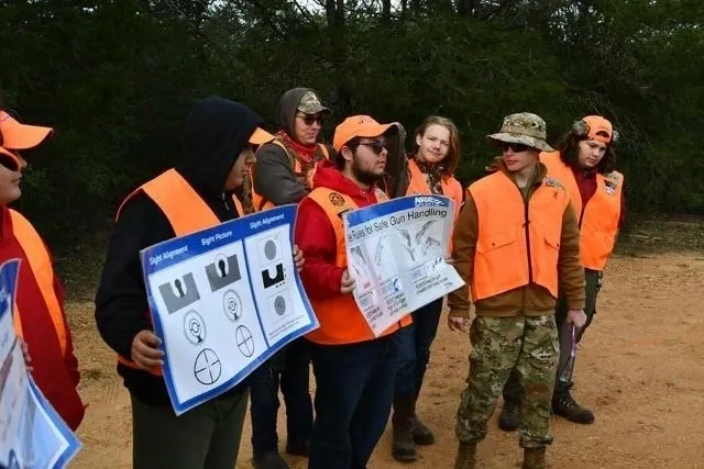 A group of people in orange vests holding up drawings.