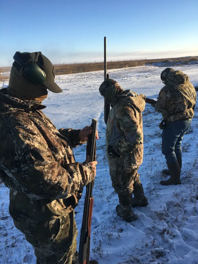 Three hunters in camouflage gear standing on a snowy field.
