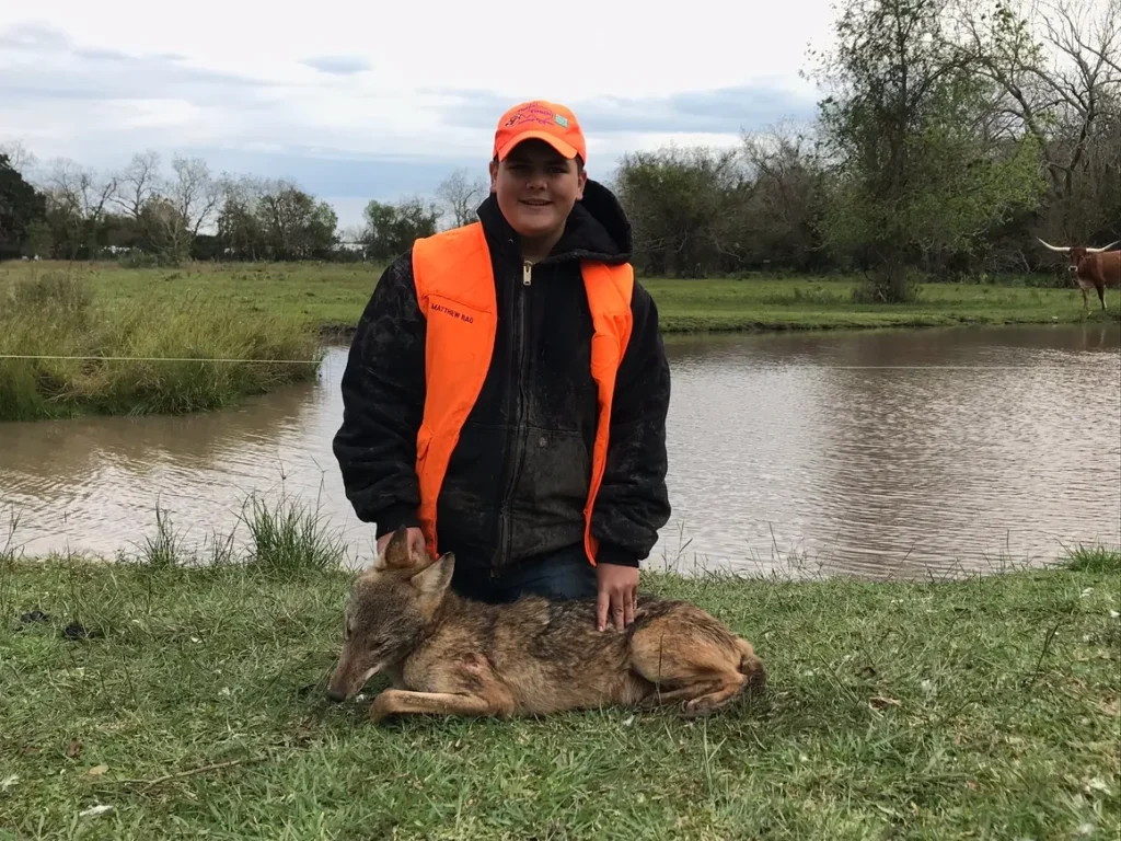 A man in an orange vest standing next to dead animals.