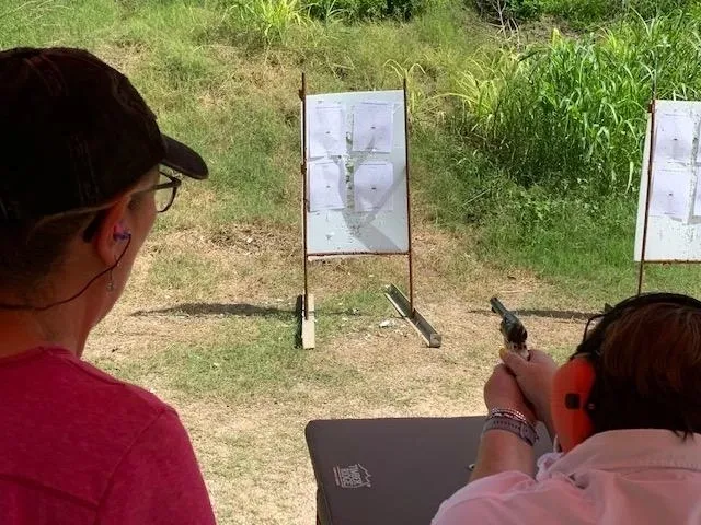 A woman is holding a gun and pointing at the target.