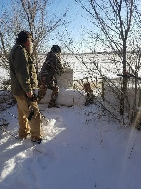 Two men in the snow near a tree.