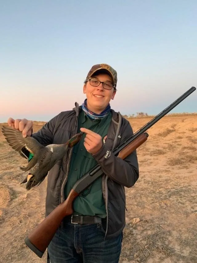 A man holding a bird and a rifle in his hands.