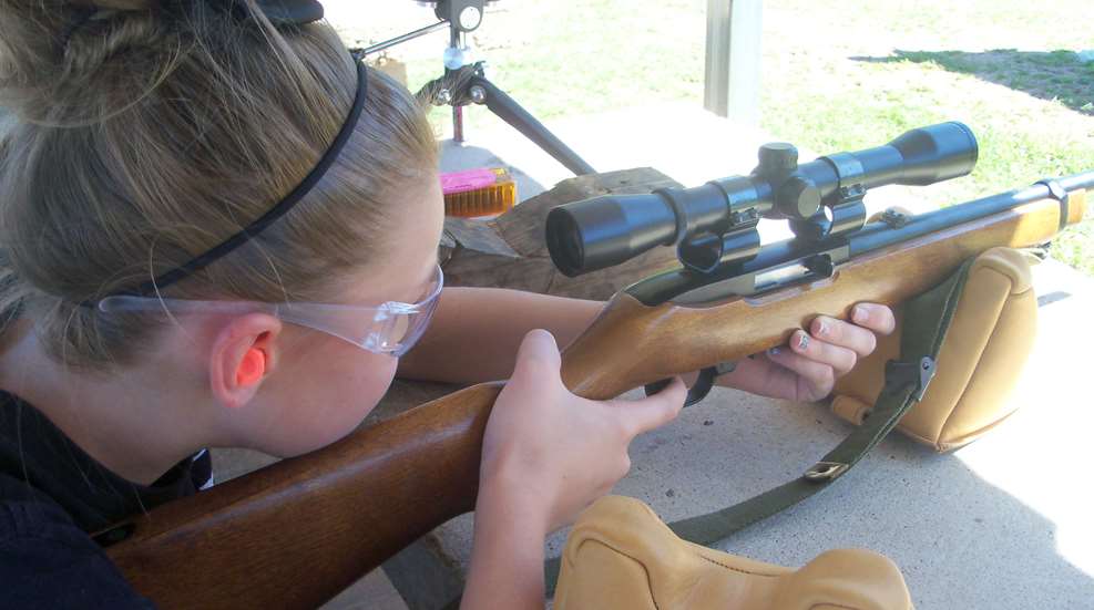 A girl is holding a rifle and aiming it.