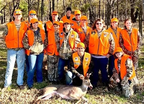 A group of people in orange vests standing next to a deer.