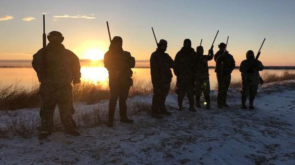 A group of people standing in the snow holding guns.