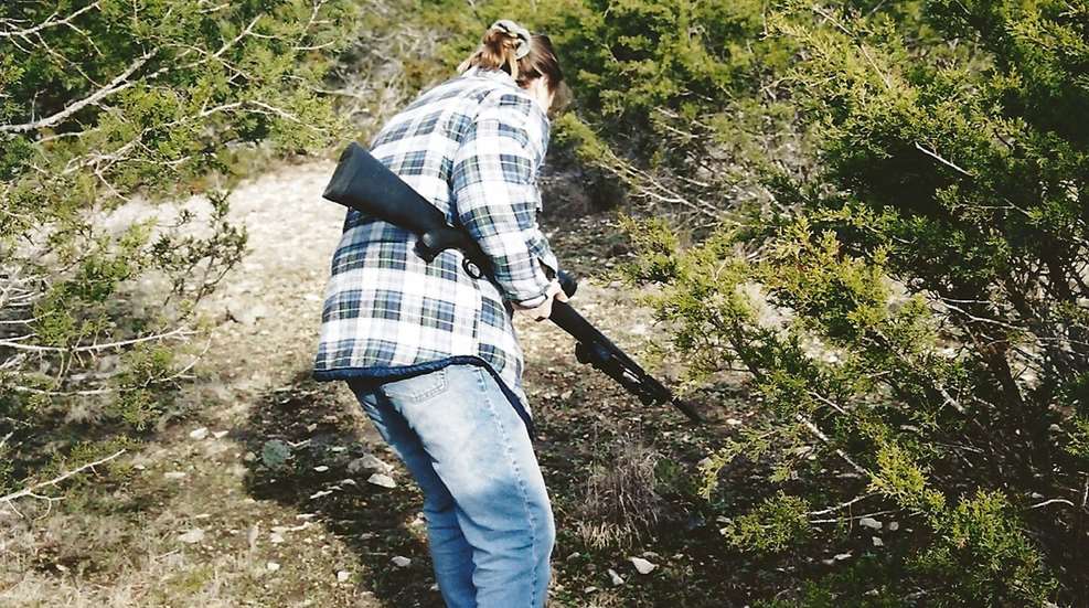 A woman is holding a gun and looking at the ground.