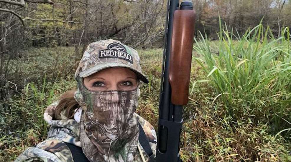 A woman in camouflage holding a rifle and wearing a hat.