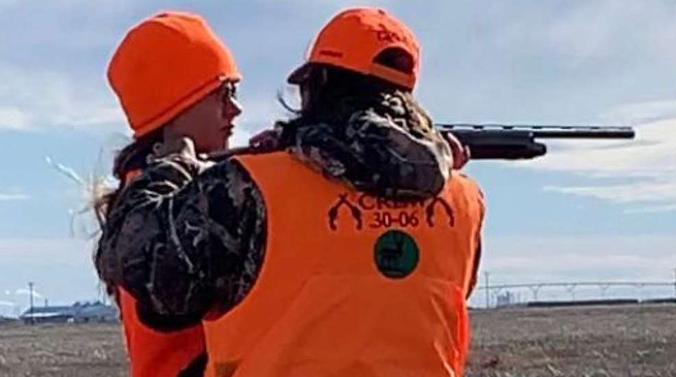 Two people in orange vests and hats are holding a gun.