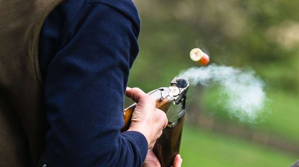 A person holding a gun and aiming at an orange.