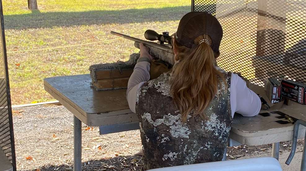 A woman is holding a rifle and aiming it.