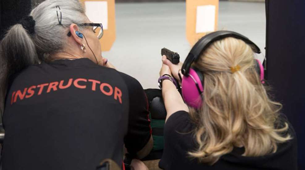A woman holding a gun while another person holds it.