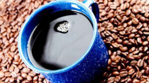 A blue cup of coffee on top of some beans.